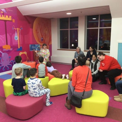 Families in Children's Room with Children's Librarian reading a story, some children in pajamas