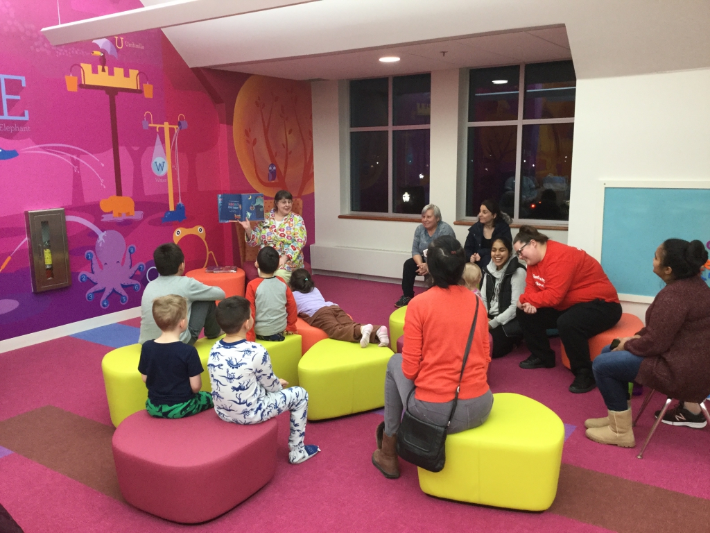 Evening PJ Storytime Families in Children's Room with Children's Librarian reading a story, some children in pajamas