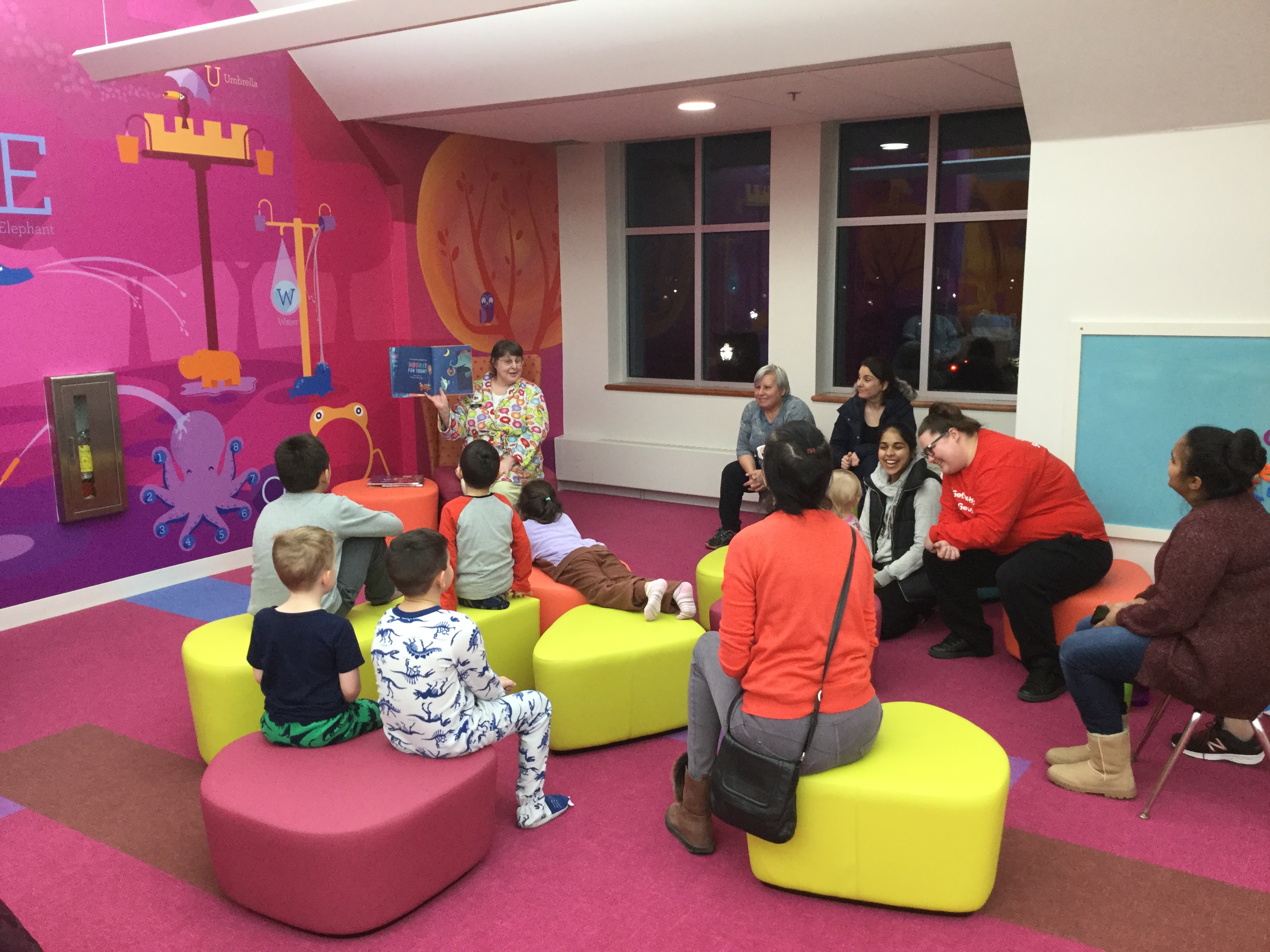 Families in Children's Room with Children's Librarian reading a story, some children in pajamas
