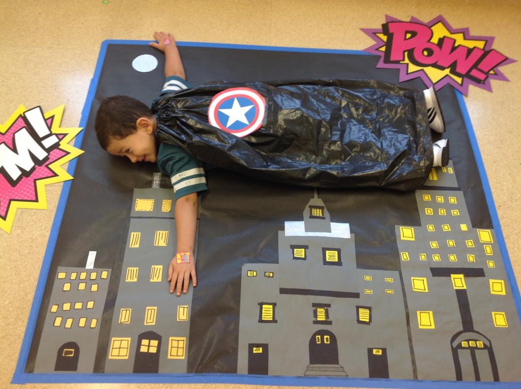 Superhero Day Young boy pretending to fly over buildings on floor mat