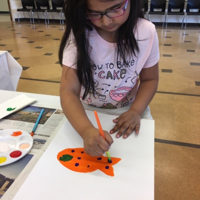 Young girl painting a fish at a table