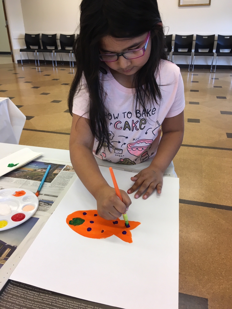 Painting to Music Young girl painting a fish at a table